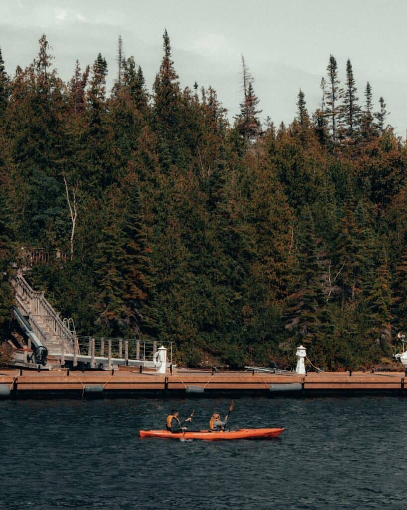 25 Jaw-Dropping Things to Do Tobermory, Ontario 12 Two people kayaking along the lake in red/orange kayaks.