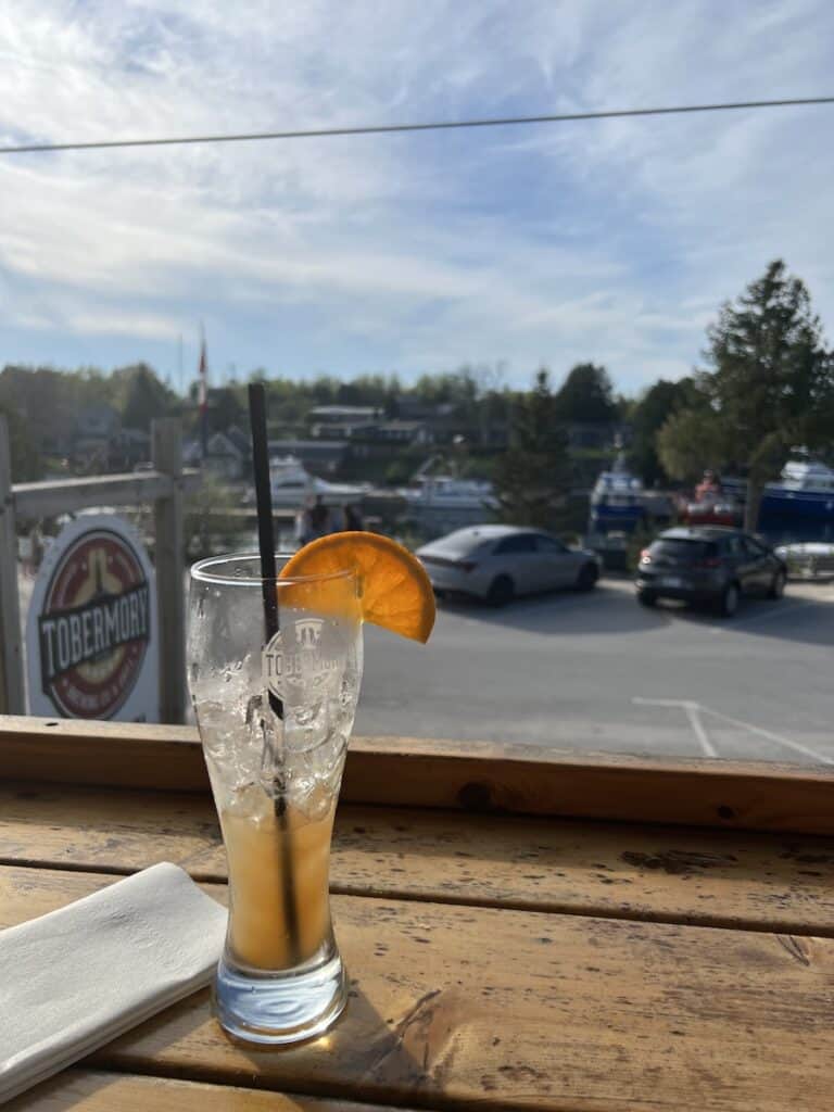 25 Jaw-Dropping Things to Do Tobermory, Ontario 15 Tobermory brewery patio with a half drunken cocktail looking out over their sign.