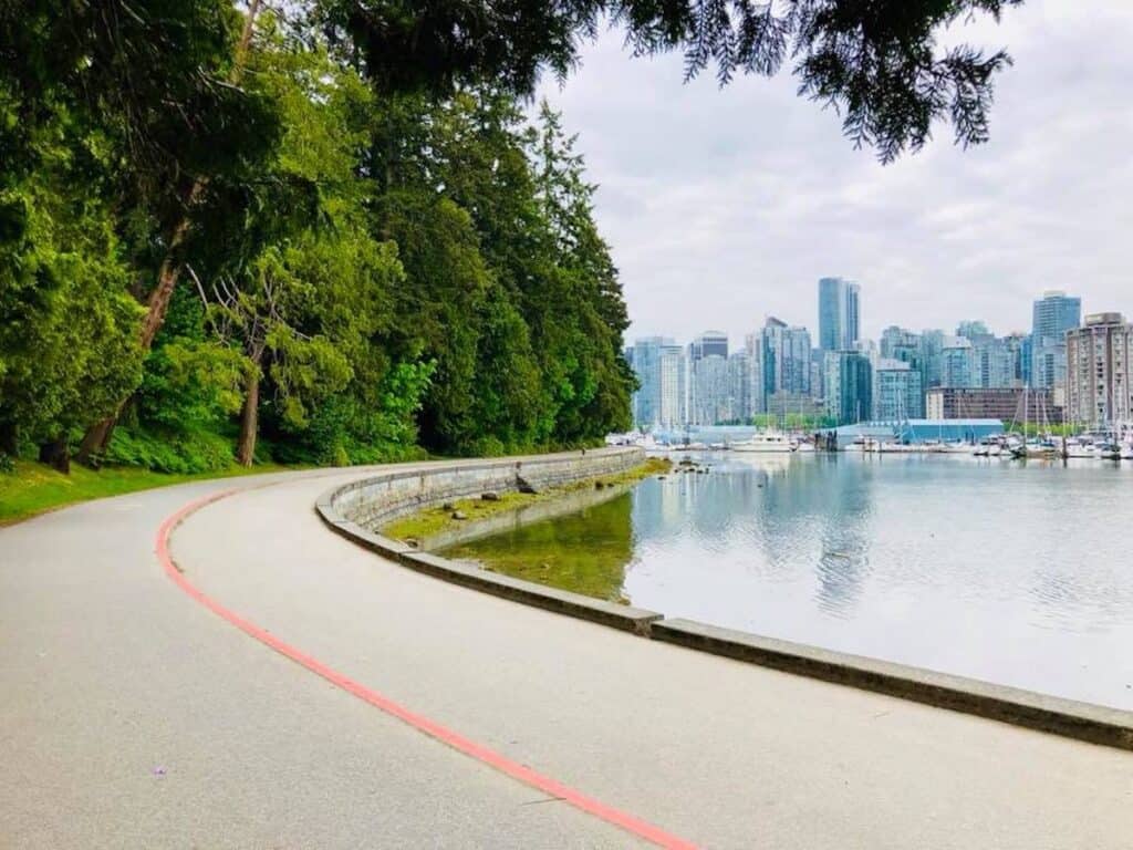 37 Amazing Vancouver Bucket List Things to Do 2 Paved pathway at Stanley Park to ride on your bicycle. View of the Vancouver skyline in the background.