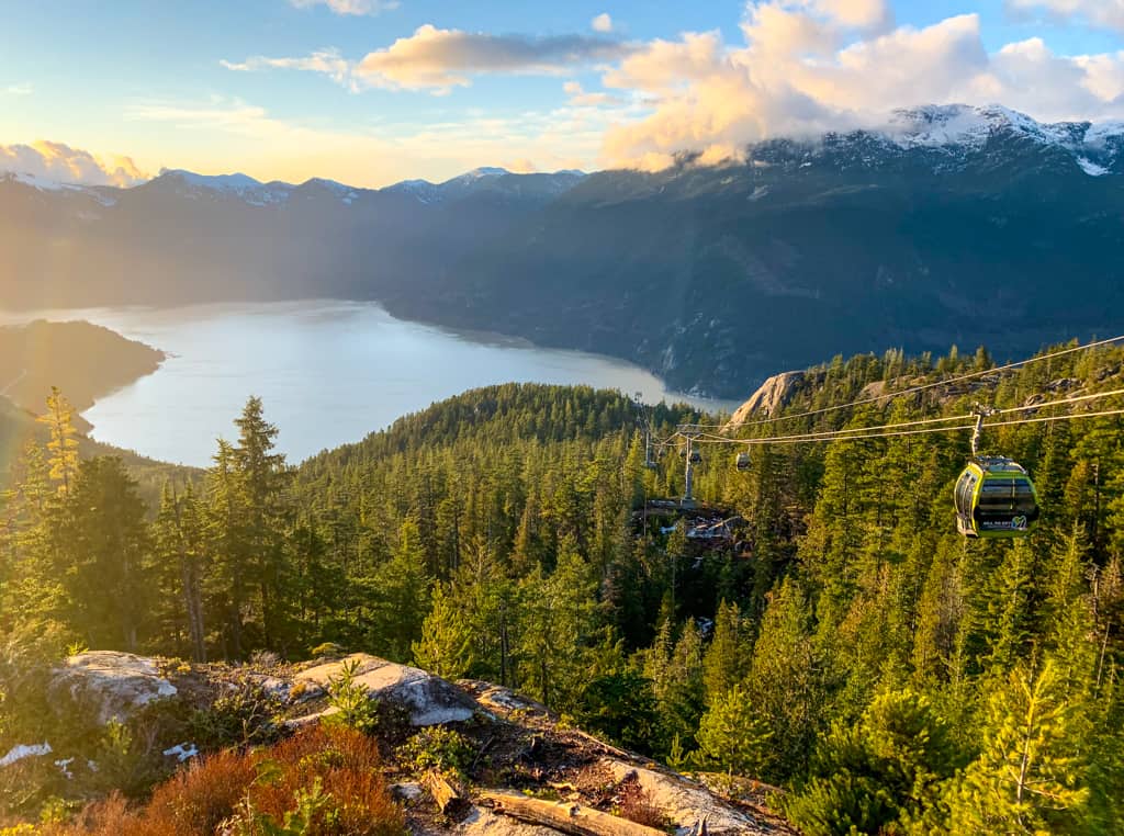 37 Amazing Vancouver Bucket List Things to Do 4 The Sea to Sky Gondola descending down the mountain through steep pine tree forests. In the background you can see the Whistler mountain and a lake. In the far distance is Vancouver.