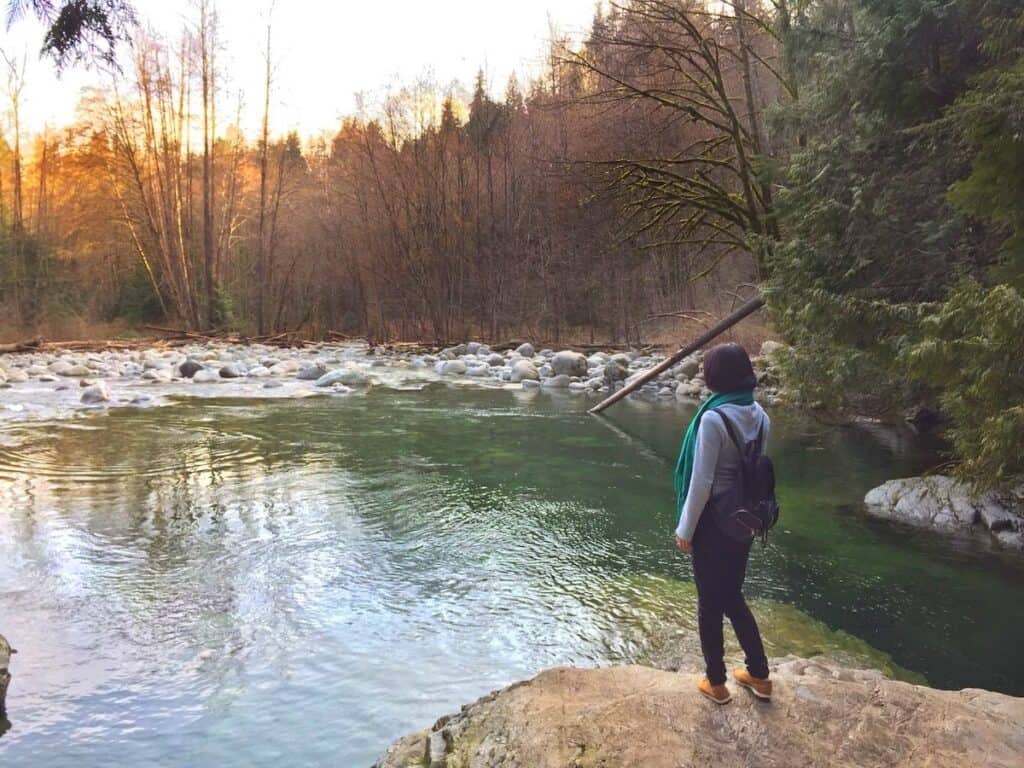 37 Amazing Vancouver Bucket List Things to Do 5 Woman looking out over a lake at Lynn Canyon Park with green waters.