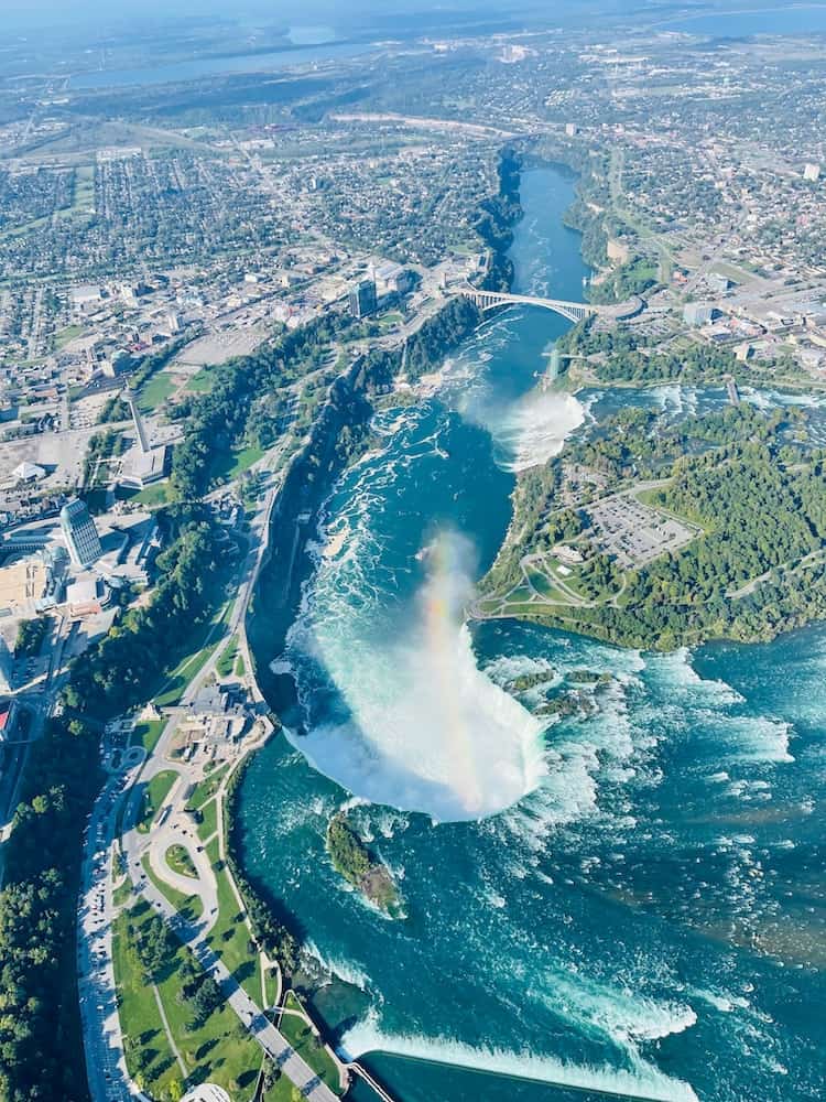 Aerial view over Niagara Falls in Canada with a rainbow coming off of the Horseshoe falls. View of the Niagara Escarpment with green trails and a pretty bridge across Niagara River.