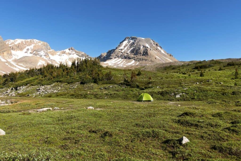 11 Epic Sites for Backcountry Camping in Canada (2024) 8 Green tent backcamping in Canada with a snowy mountain peak in the back.
