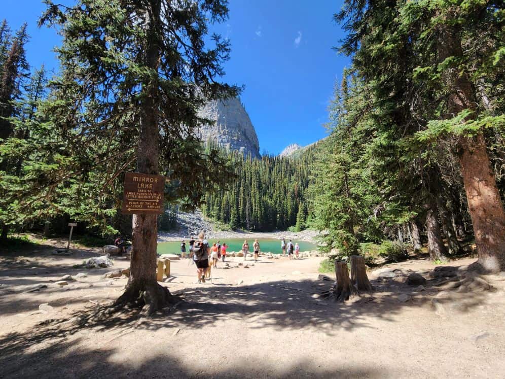 19 Best Hikes in Banff National Park (2024 Guide) 17 People milling about an emerald lake beside sgns for hiking directions in Banff National Park.