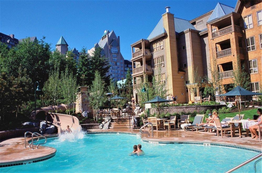 11 Best Resorts in Whistler (2024 Guide) 11 Brown wood siding of the Embarc Whistler resort in the background with an outdoor pool and waterslide in the foreground.