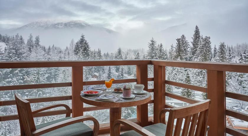 11 Best Resorts in Whistler (2024 Guide) 4 Two wooden chairs with a table on a wooden balcony overlooking the snowcapped pine trees of Whistler at the Four Season Resort Whistler.