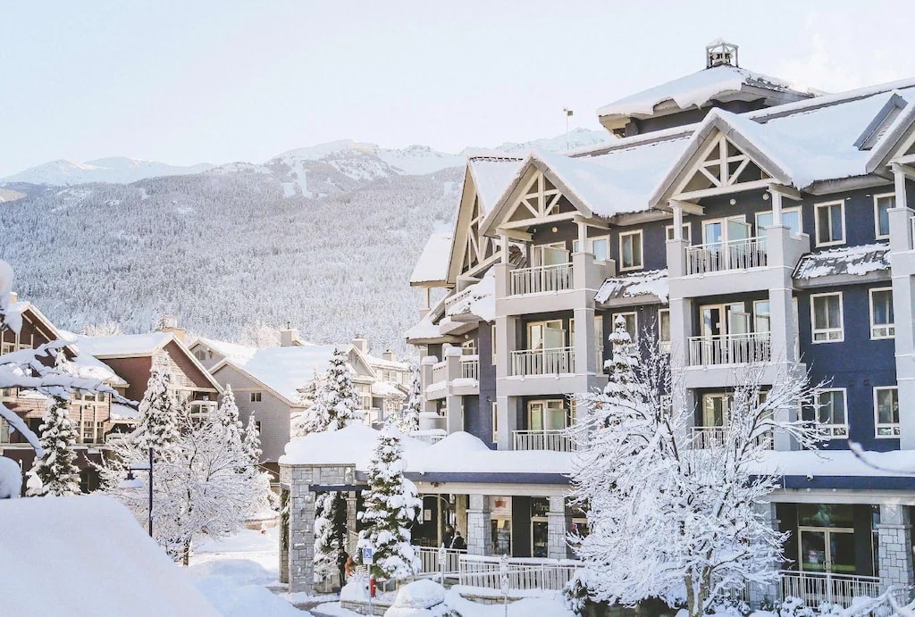 11 Best Resorts in Whistler (2024 Guide) 6 Snowy summit lodge boutique hotel with the blue siding standing out against the white capped mountains in the background.