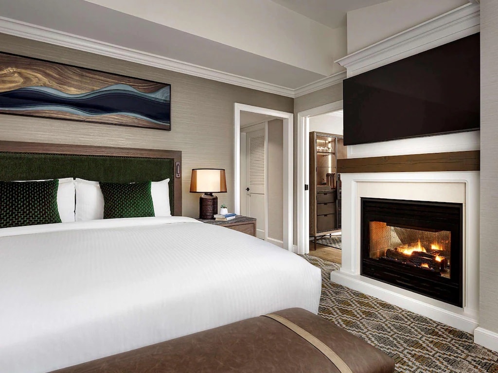 11 Best Resorts in Whistler (2024 Guide) 1 Fairmont Chateau in Whistler room with green throw pillow on a white bed and a fireplace in the room.