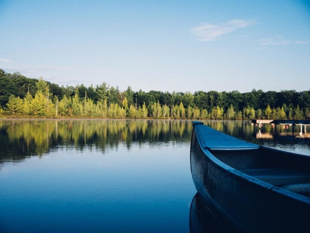 Banff National Park Itinerary: 1, 3, and 5 Day Guides 22 A boat on Herbert Lake in Banff with blue calm water and green trees on the other side.
