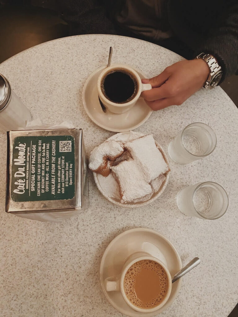 17 Pros and Cons of Living in New Orleans in 2024 1 A man holding a cup of black coffee and a couple of bagels on a ceramic table in one of the cafes in New Orleans - the food scene is a great plus of living in New Orleans.