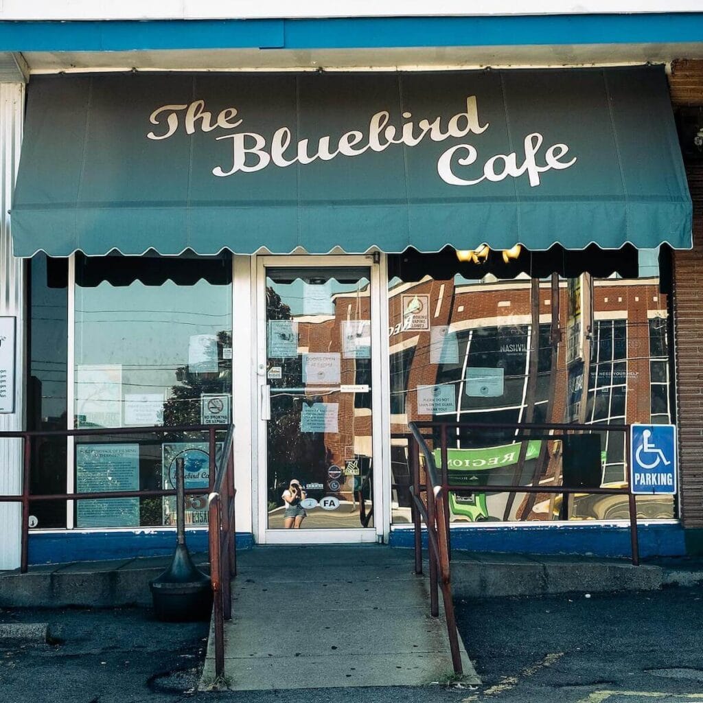 23 Pros and Cons of Living in Nashville in 2024 1 Front view of The Bluebird Cafe taken by a girl with her reflection in the glass door mirror of the cafe.