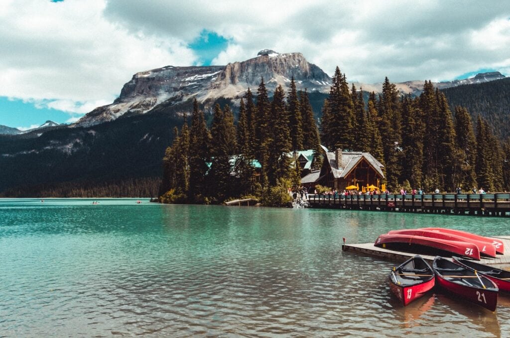 Banff National Park Itinerary: 1, 3, and 5 Day Guides 17 A couple of kayaks at a jetty at the front of the image with a large cabin house in the middle of the Emerald Lake and mountains at the back.