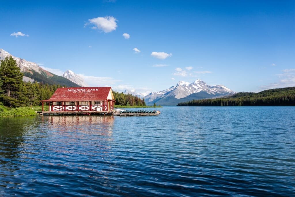 Banff National Park Itinerary: 1, 3, and 5 Day Guides 14 Blue lake with a red-roof cottage on a dock in Jasper National Park under a clear blue sky.