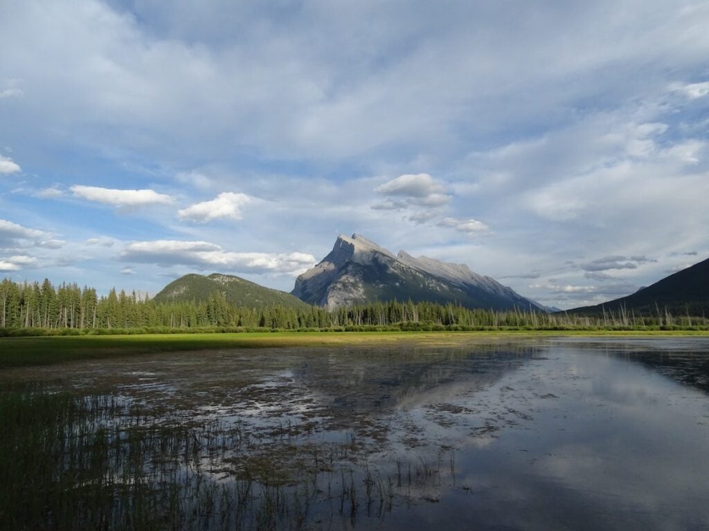 Banff National Park Itinerary: 1, 3, and 5 Day Guides 8 Green lake in Banff surrounded by green trees and mountains on a cloudy day.