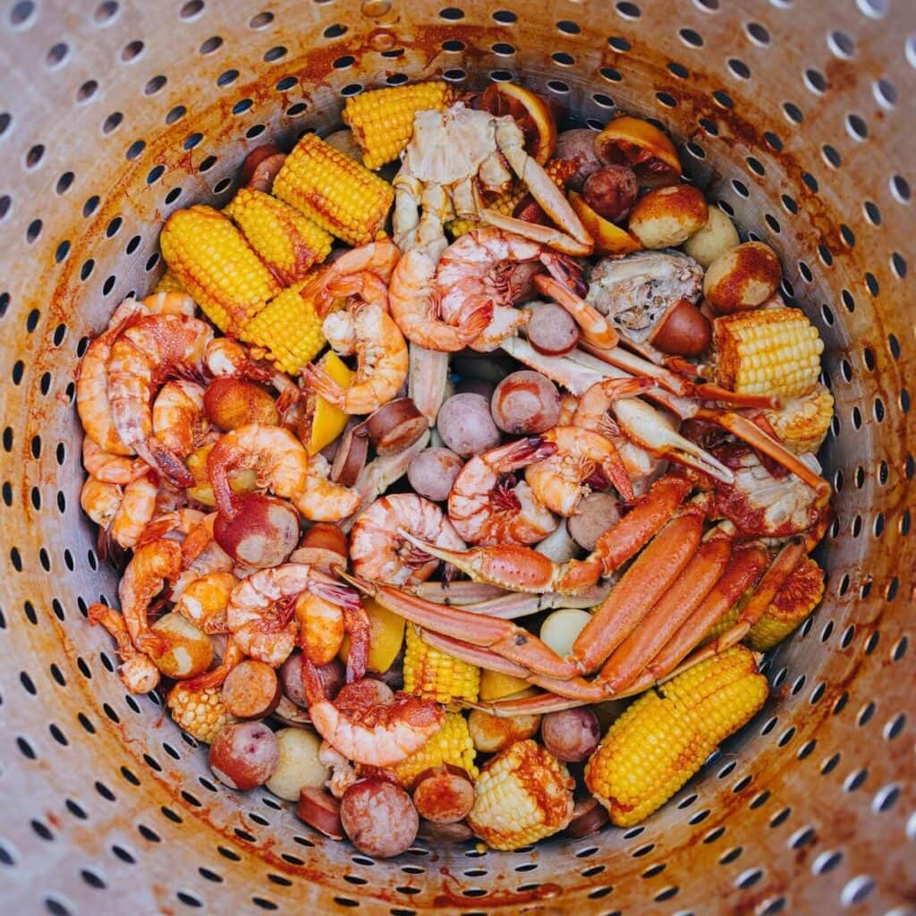 27 Pros and Cons of Living in South Carolina in 2024 3 A metal basket is full of cooked seafood like crabs and shrimp with corn - the food in South Carolina is a big pro when deciding to move there.