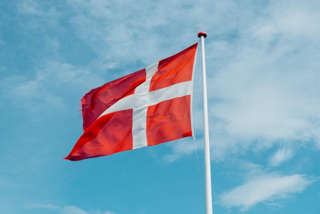 23 Pros and Cons of Living in Denmark in 2024 1 The national flag of Denmark is on a white pole under a beautiful blue sky.