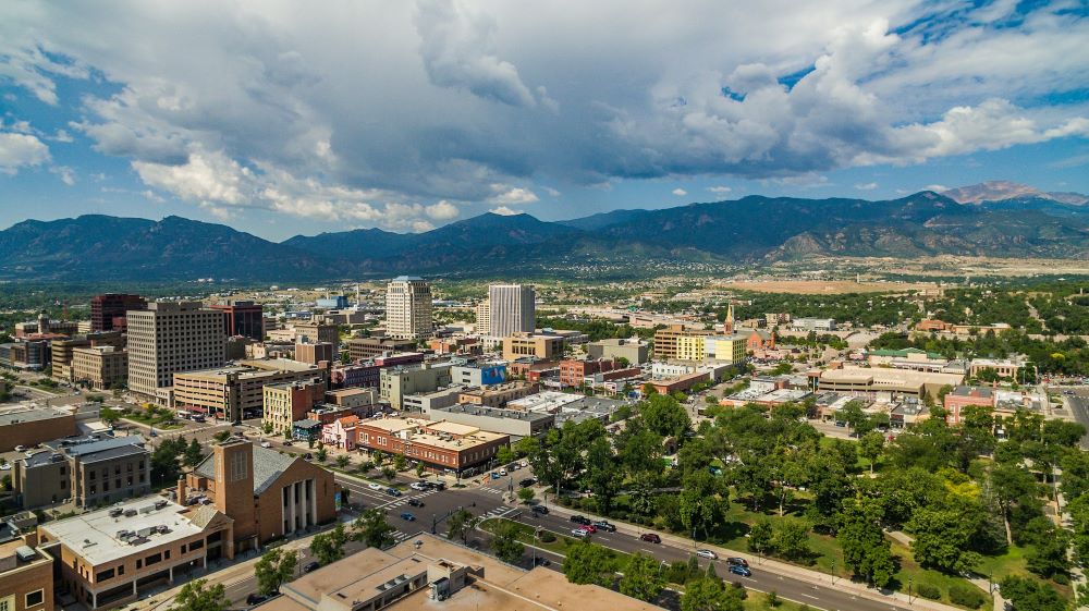 23 Pros and Cons of Living in Colorado Springs in 2024 2 An aerial view of downtown Colorado Springs, overlooking Acacia Park at the intersection of Nevada Ave. and E Bijou St. with Pikes Peak in the distance.