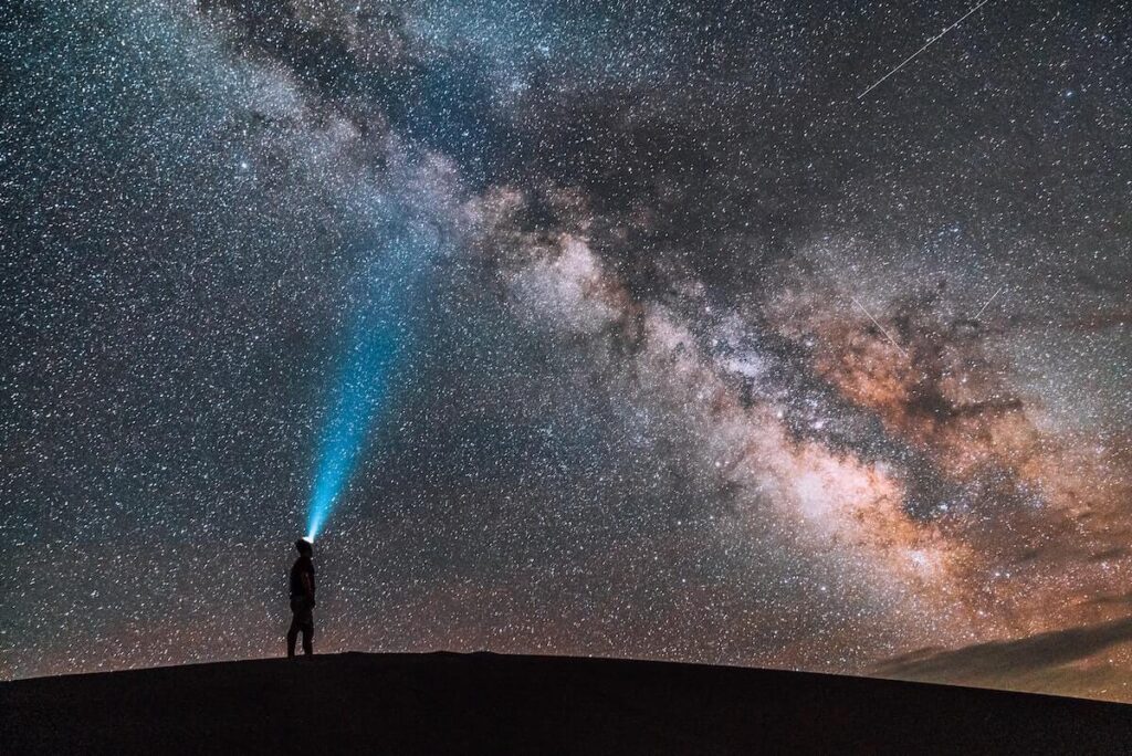 19 Pros and Cons of Living in Colorado in 2024 5 A man with a headlight standing on top of a mountain looking at the beautiful night sky.