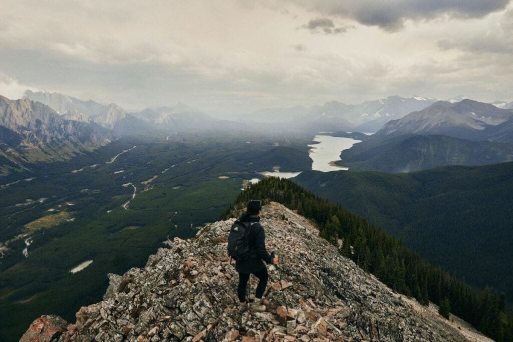 5 Best Banff Helicopter Tours (2024) 5 A person hiking at the top of the mountain showing the panoramic view of the mountains and lake of Banff NP.
