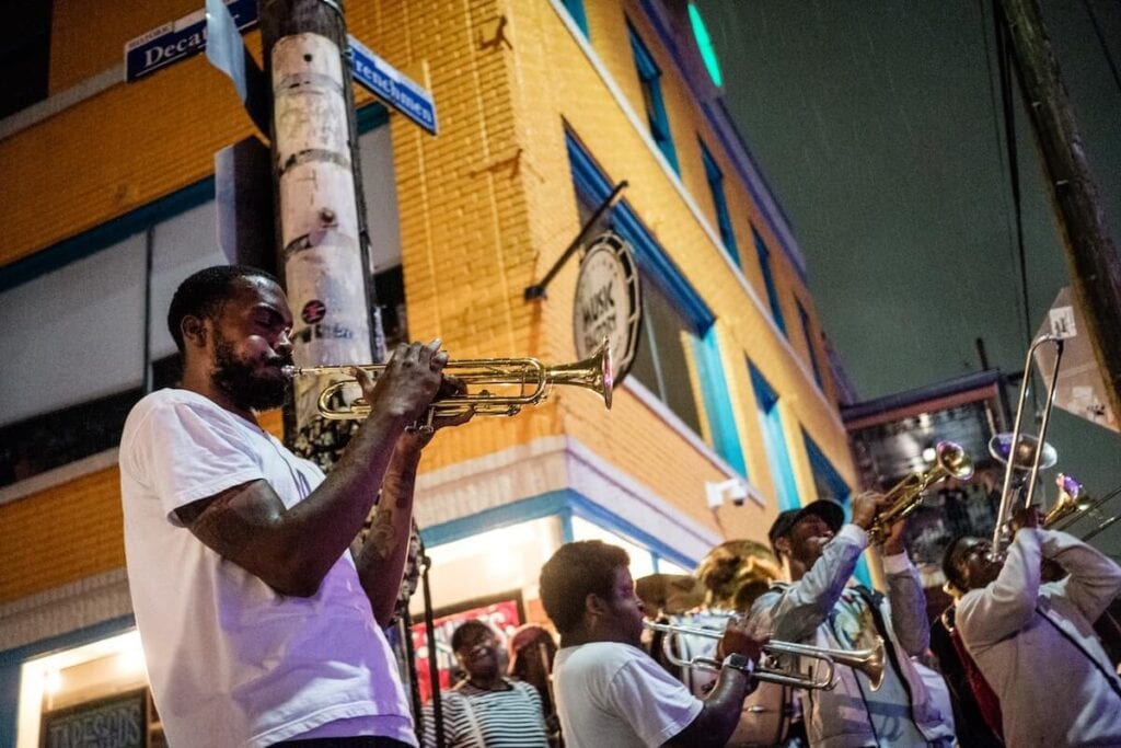 17 Pros and Cons of Living in New Orleans in 2024 2 A band playing their trumpets on one of the corner streets in New Orleans under the night sky.