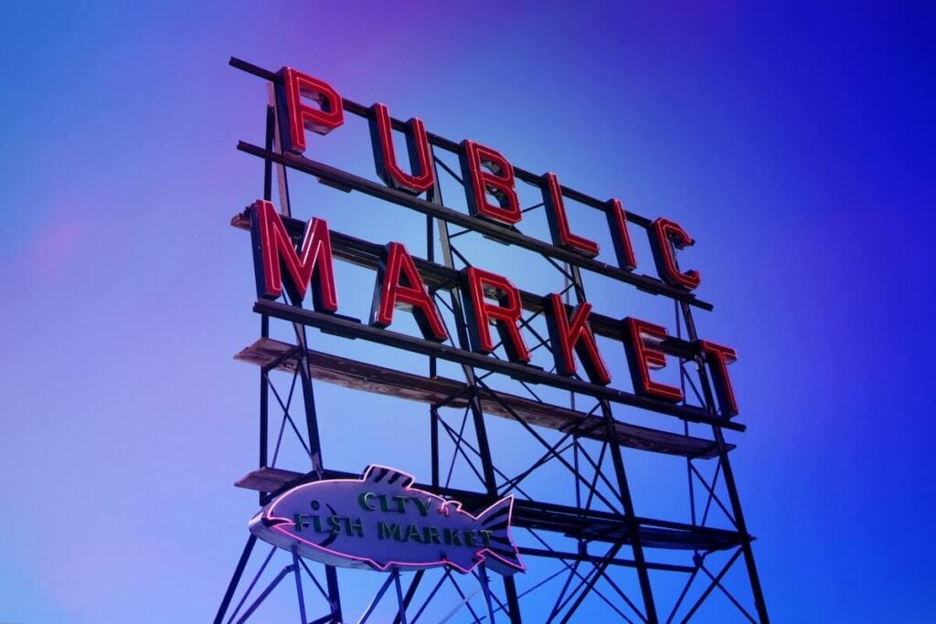 23 Pros and Cons of Living in Seattle in 2024 2 Huge signage of a public market in Seattle under a blue sky.