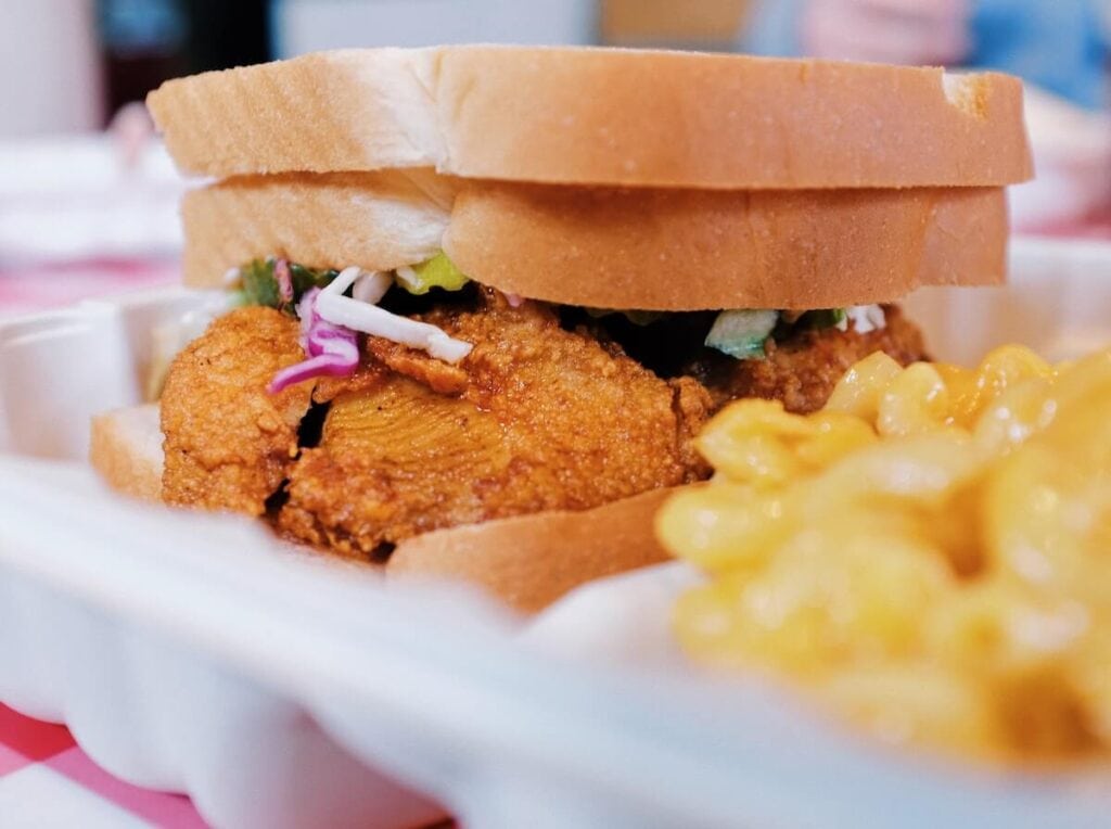 23 Pros and Cons of Living in Nashville in 2024 2 A photo of a fully loaded chicken sandwich meal filled with sliced onions and pickles - one of the pros of living in Nashville, hot fried chicken everywhere!