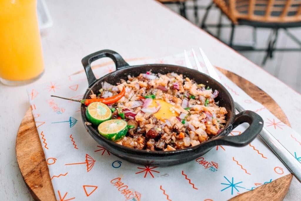 21 Pros and Cons of Living in the Philippines in 2024 4 Sizzling meat with lots of chopped onions topped with an egg on a sizzling plate on top of a white table in one of the restaurants in the Philippines.