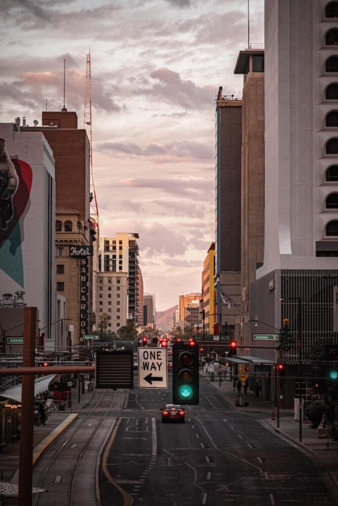 29 Pros and Cons of Living in Phoenix, Arizona 4 The green light on the stoplight in the middle of the road in Phoenix is surrounded by tall buildings on a beautiful afternoon.