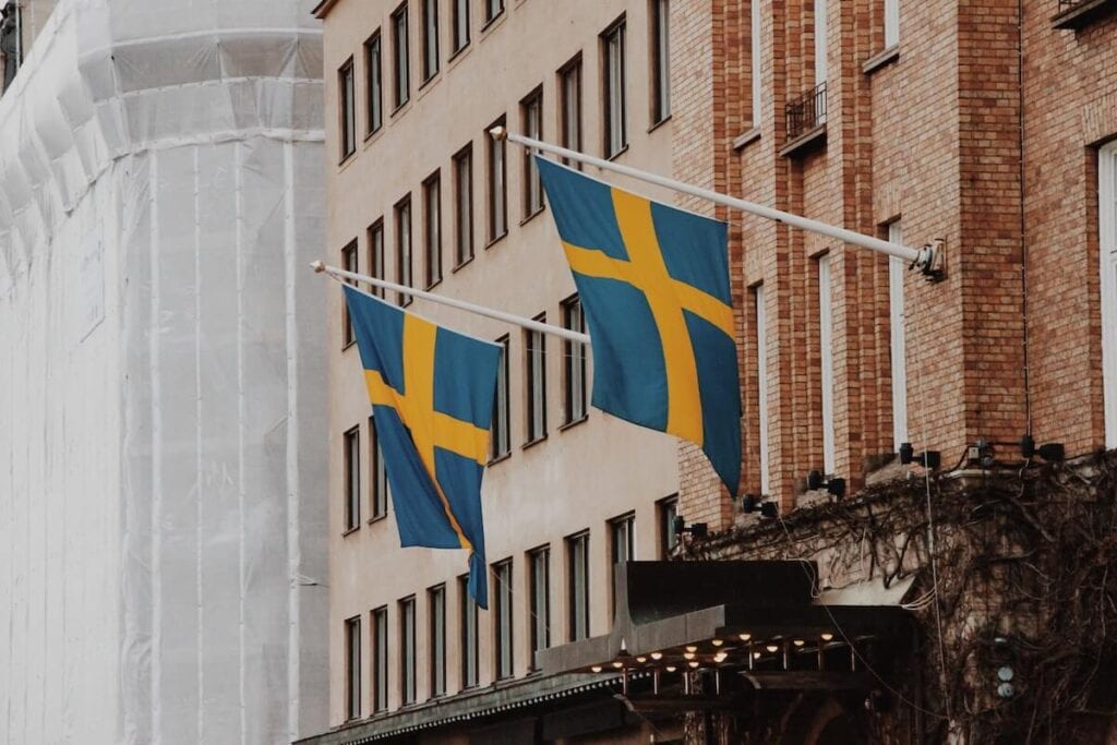 27 Pros and Cons of Living in Sweden in 2024 2 Two Swedish flags are attached to poles in a brown building in Sweden.