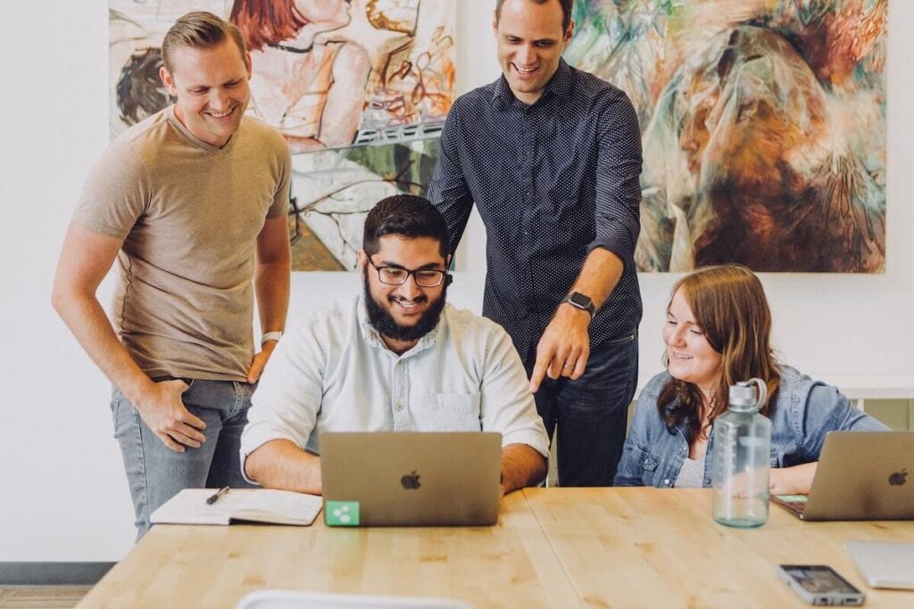 16 Pros and Cons of Living in Iowa 2024 3 A team consisting of four people huddle up and checks their work on a laptop in an office in Iowa.