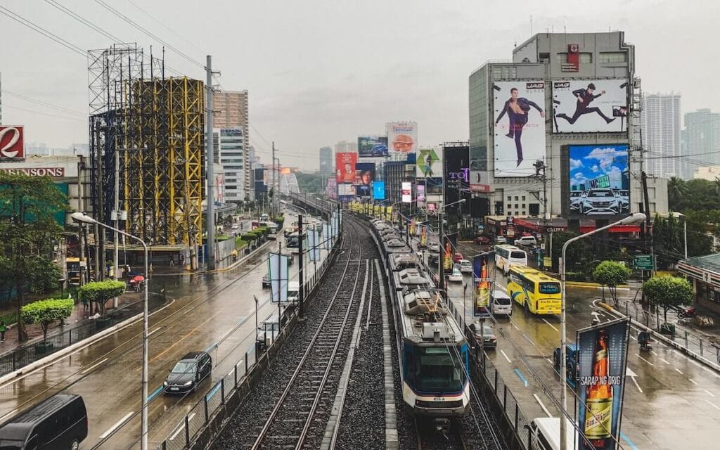 21 Pros and Cons of Living in the Philippines in 2024 2 A train on the railway in one of the cities in the Philippines surrounded by cars and buildings on a rainy day.