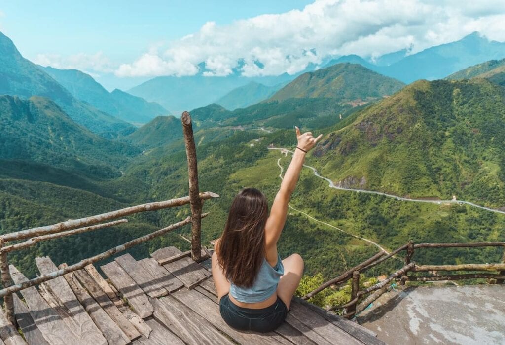 23 Pros and Cons of Living in Vietnam in 2024 4 A woman raising her hand facing a beautiful view of the mountains of Vietnam on a sunny day.