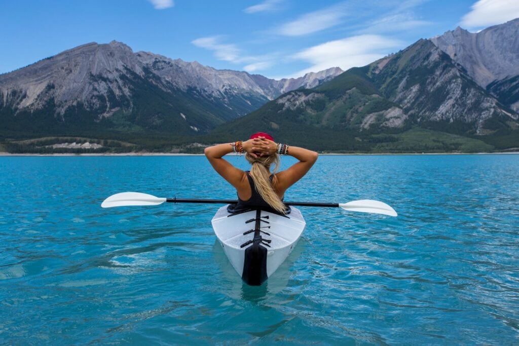 Where to Stay in Lake Louise Canada: 14 Best Hotels (2024) 11 Woman riding a kayak in the middle of a lake looking at the mountains