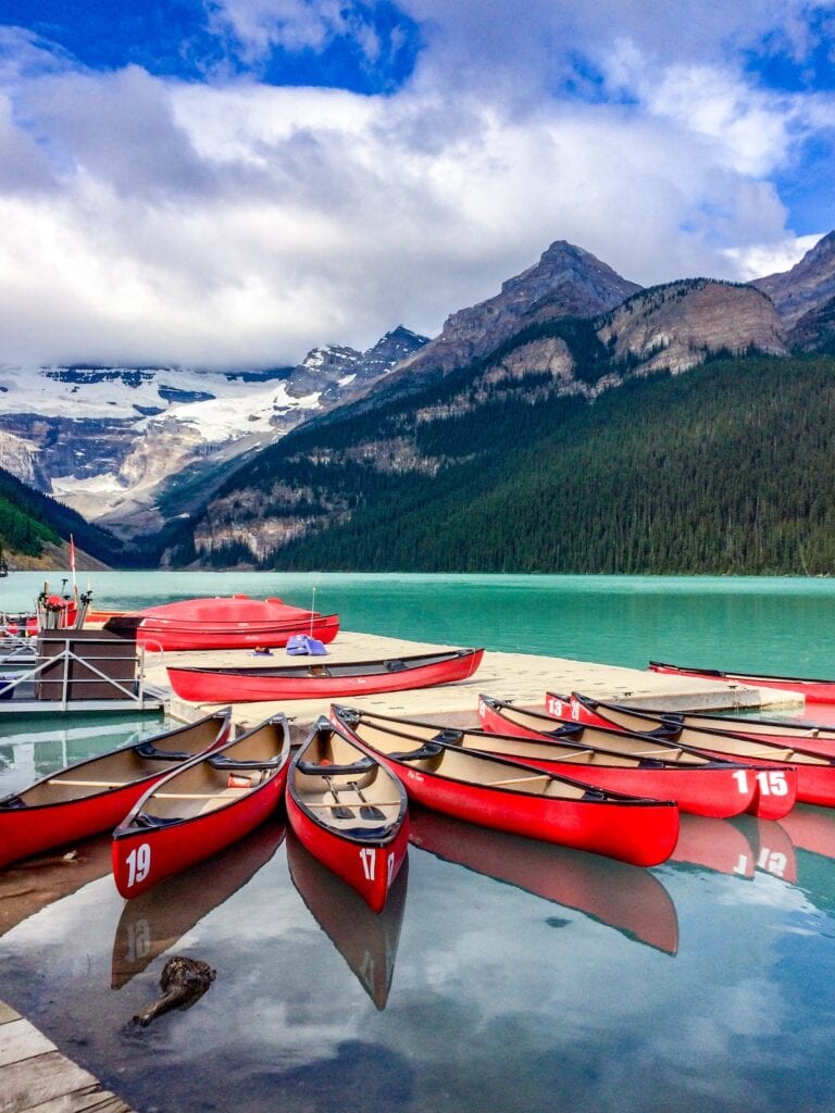 Where to Stay in Lake Louise Canada: 14 Best Hotels (2024) 7 A group of red canoes sitting on top of lake on a dock. The lake is near mountain ranges nd green forests. This is in The Baker Creek mountain Resort, one of the bests hotels to stay in Lake Louise.