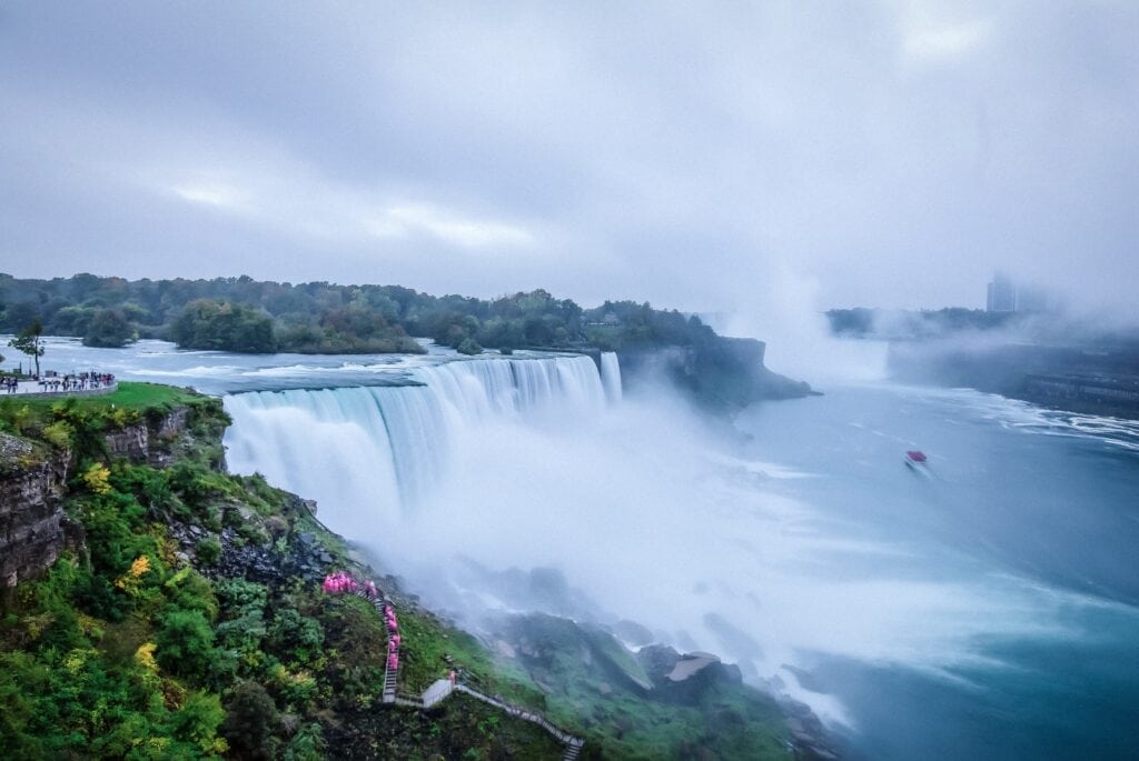 11 Awesome New York Niagara Falls Tours (2024) 8 Water falling off a large cliff creating a large waterfall near large green body of land. This is thew view on the New York Niagara Falls Tout.