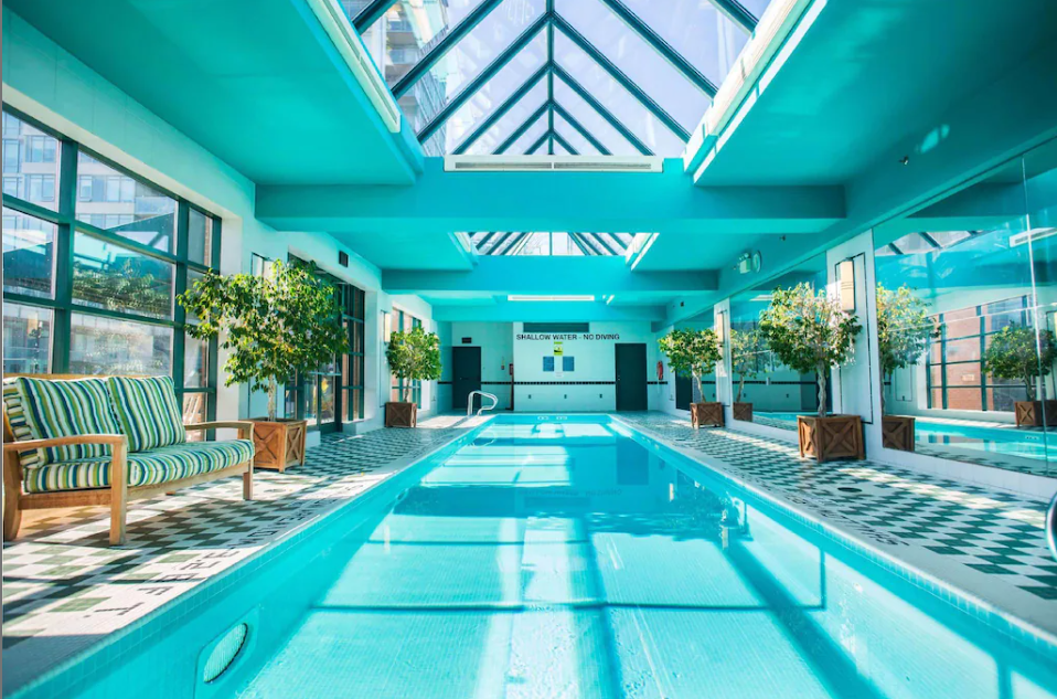 12 Best Toronto Hotels With Rooftop Pools (2024) 4 A long indoor rooftop pool with a comfortable two-person chair beside it. It is under a transparent roof in the Yorkville Sonesta Hotel Toronto.
