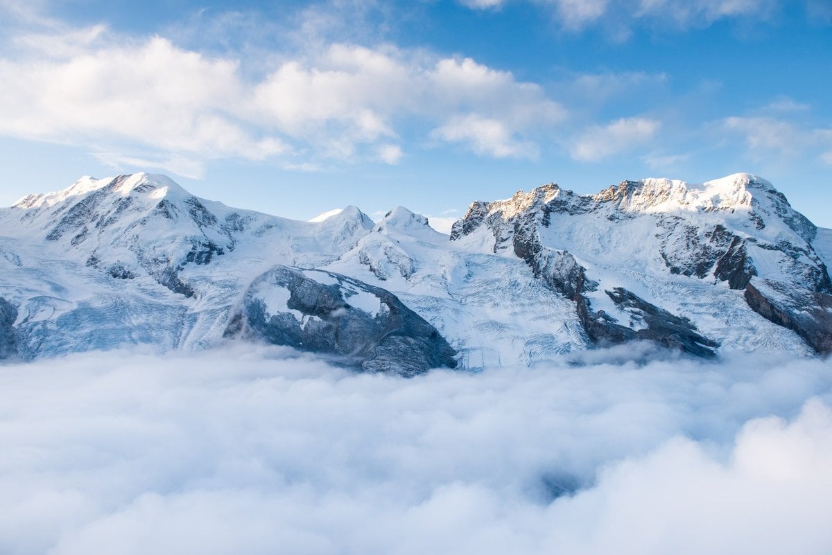 12 Best Jasper Helicopter Tours (2024) 14 Large mountain covered with snow lined up under a cloudy blue sky during the daytime. This is the Mt. Columbia Mountaintop, one of the destinations of the best helicopter tours in Jasperr.