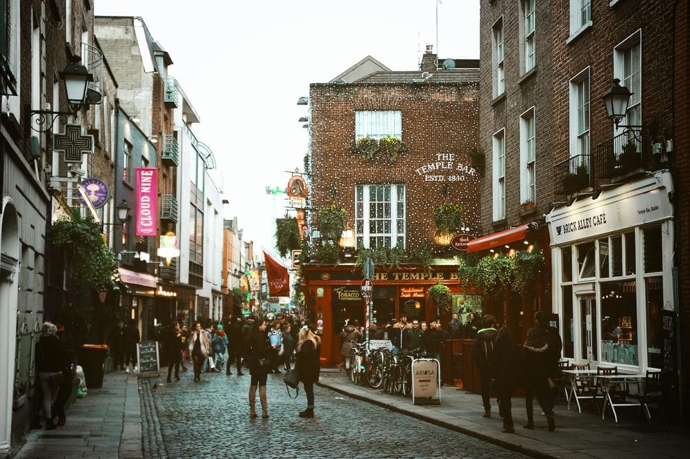 Living In Dublin 2024: The Complete Expat Guide 1 Several people standing on a street near brown buildings and cafes. One of the great things about living in Dublin is its walkable destinations and welcoming people.