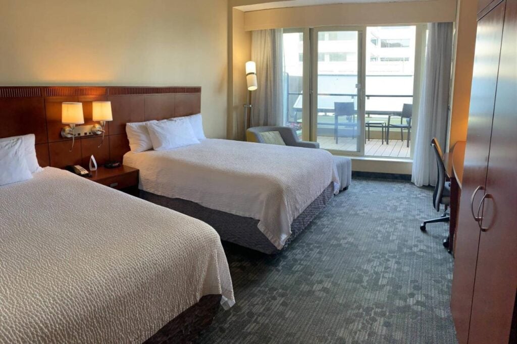 Where to Stay in Halifax: 17 Best Hotels in 2024 6 Two beds with white sheets inside a room with a balcony. A cabinet, a desk, and a swivel chair can also be seen on the side. This is one of the rooms from Courtyard by Marriott Halifax.