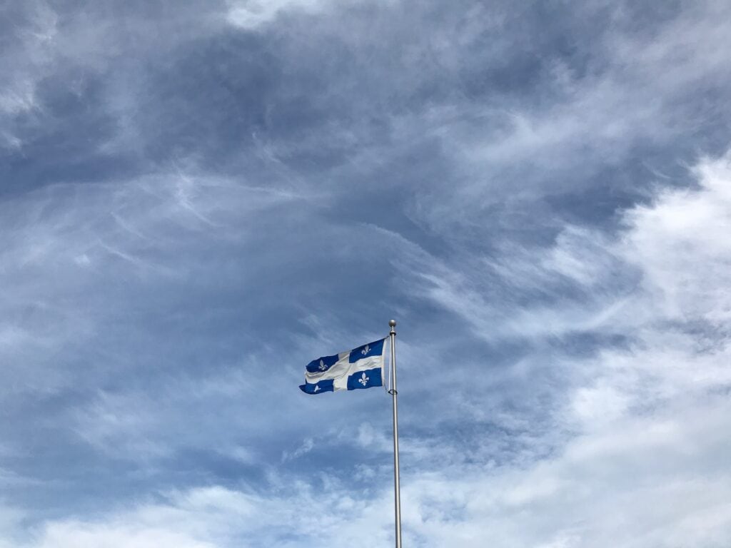 Whale Watching in Quebec: 9 Best Tours in 2024 11 A photo of a blue and white colored flag under the blue cloudy sky. This is the Quebec National Flag. Quebec is a great place for whale watching tours.