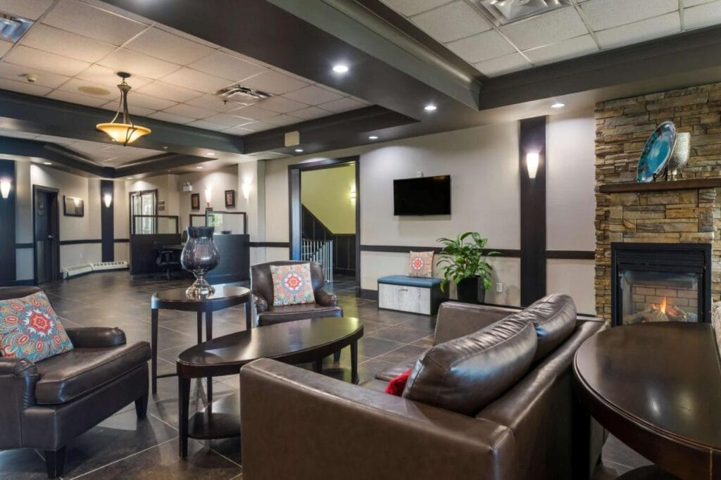 Where to Stay in Halifax: 17 Best Hotels in 2024 12 A photo of a brown couch set with brown coffee tables inside a well-lit room with brown and white walls. A fireplace is also placed beside the large couch. This is the welcoming are of the Best Western Plus Chocolate Lake Hotel.