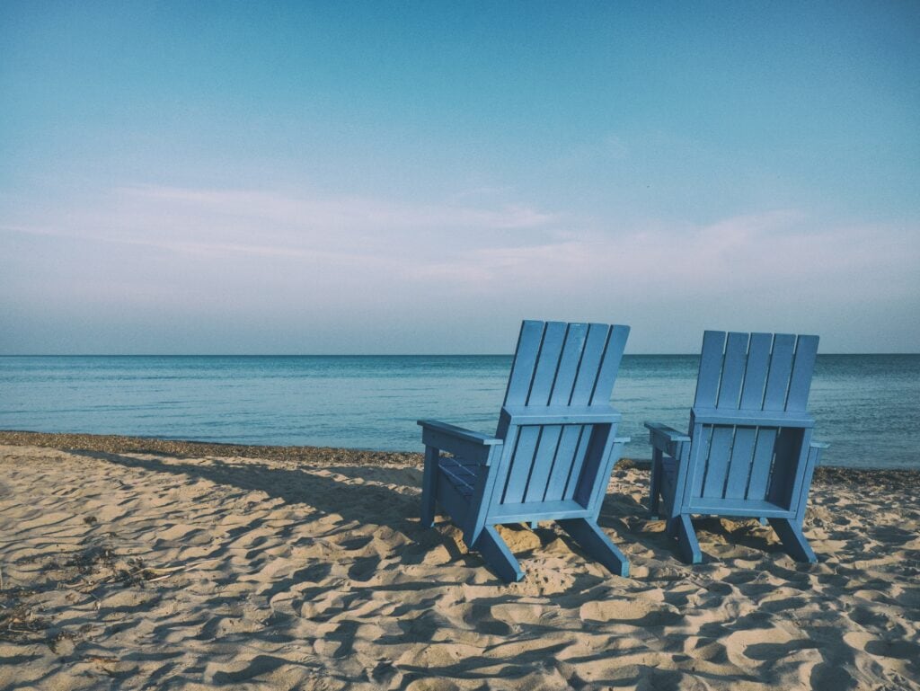 25 Pros and Cons of Living in Costa Rica in 2024 10 Two blue Adirondak chairs beside the ocean in Costa Rica with sandy beaches.
