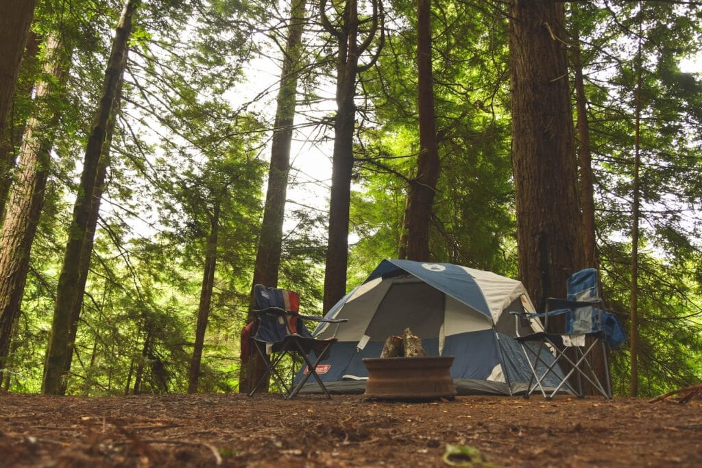 Where to Stay Near Jasper National Park: 16 Best Hotels 17 Two blue camping chairs near a camping tent in the middle of the woods. A round container in the middle of the chairs is filled with wood for a bonfire. This is the Whistler's Campground.