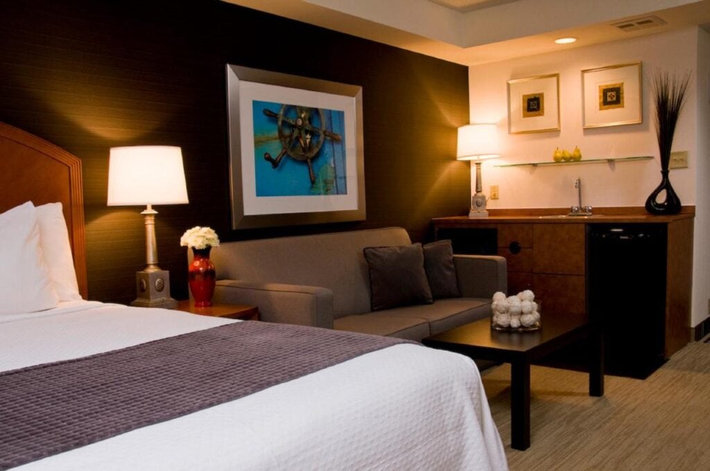 Where to Stay in Halifax: 17 Best Hotels in 2024 10 A large bed with white and grey sheets inside a room with black and white walls. A large picture frame is placed above the sofa beside the bed. A coffee table, a sink, and a lamp can also be seen on the side. This iss one of the rooms in Cambridge Suites, one of the best places to stay in Halifax.