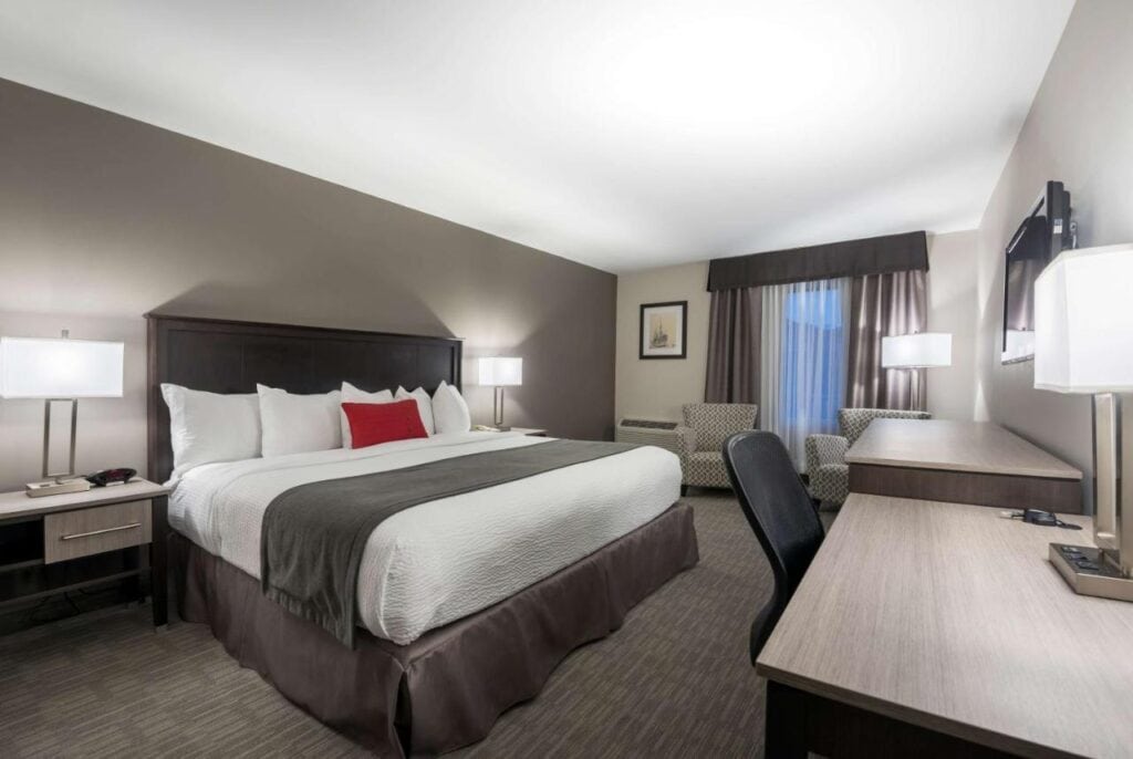 Where to Stay in Halifax: 17 Best Hotels in 2024 13 A large bed with white and gray sheets placed in the middle of a room with gray walls. Two desks with a swivel chair can also be seen near the wall. A TV is also mounted to the wall. This is one of the rooms in Chateau Bedford, Halifax.