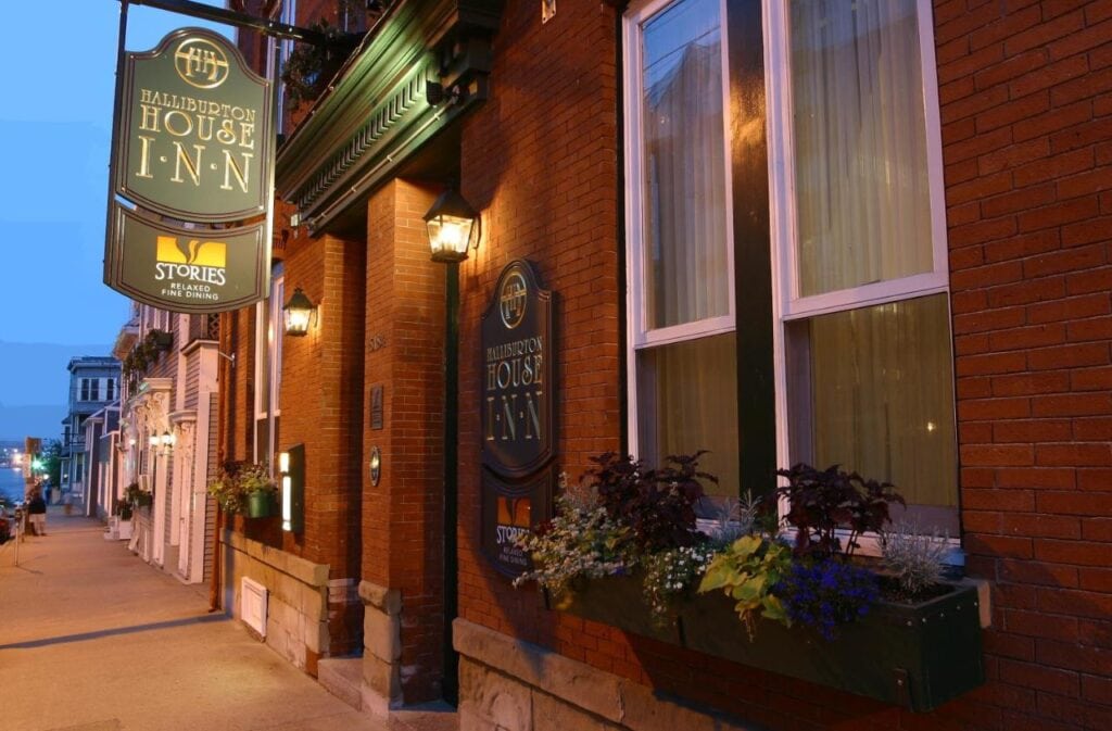 Where to Stay in Halifax: 17 Best Hotels in 2024 9 A close-up photo of a bricked building with two white windows. There is also a hanging sign that says "Halliburton House Inn" near the pillared entrance. This the Halliburton, one of the best hotels in Halifax.