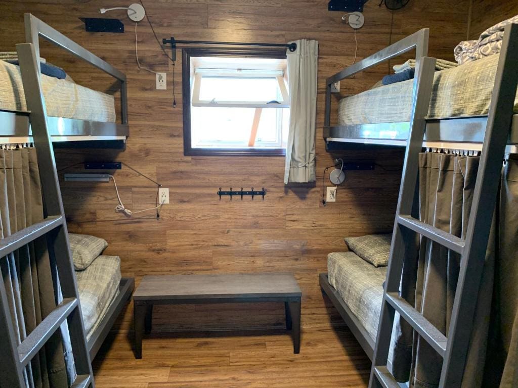 Where to Stay Near Jasper National Park: 16 Best Hotels 12 Two bunk beds with a bench in the middle. Wooden walls suround the room and small window can be seen in the middle of both beds.