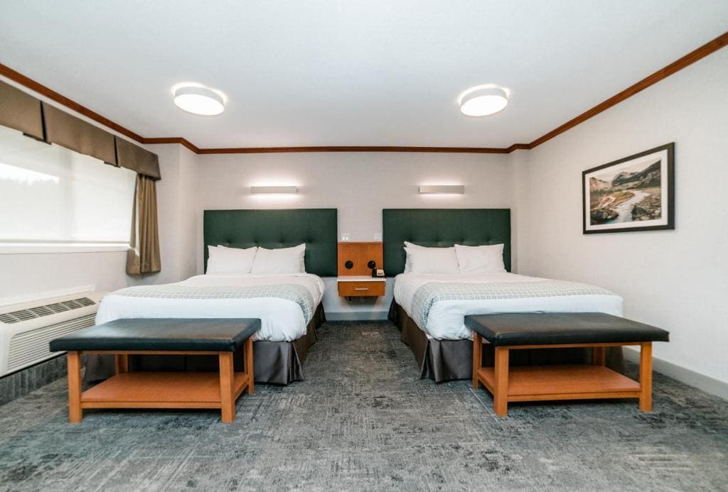Where to Stay Near Jasper National Park: 16 Best Hotels 7 Two twin sized bed in the middle of a room with white colored walls and a gray carpeted floor. A wide window can be seen beside one bed and a painting on the other. This is in Mount Robson Inn in Jasper, Alberta