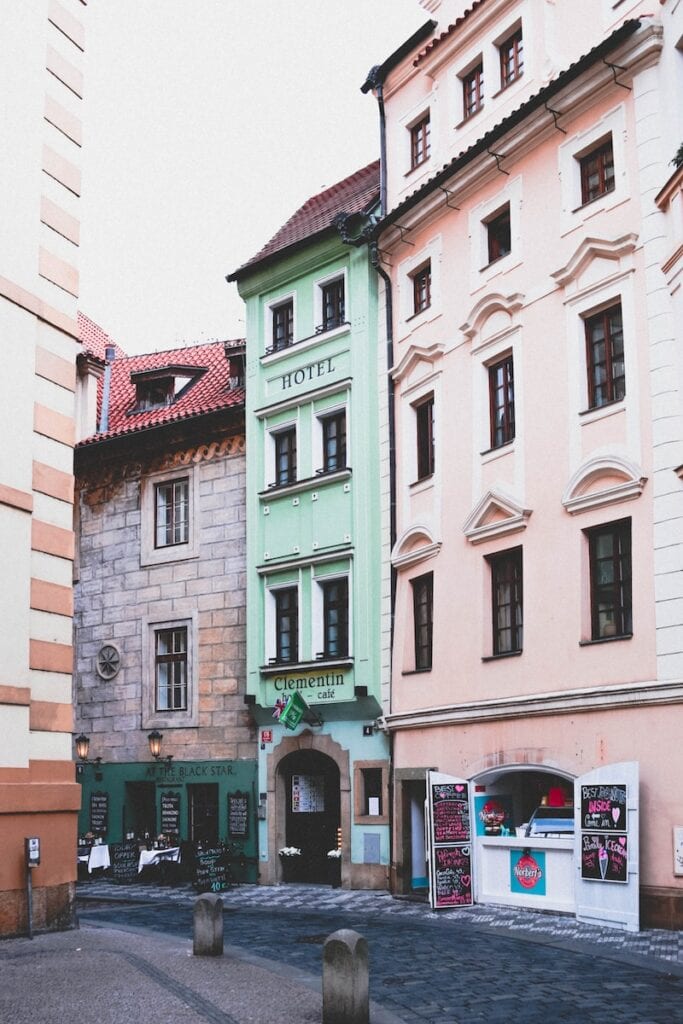 Living in Prague: The Complete Expat Guide (2024) 3 Three-storey green and beige buildings near a bricked road. These are hotels in Prague.