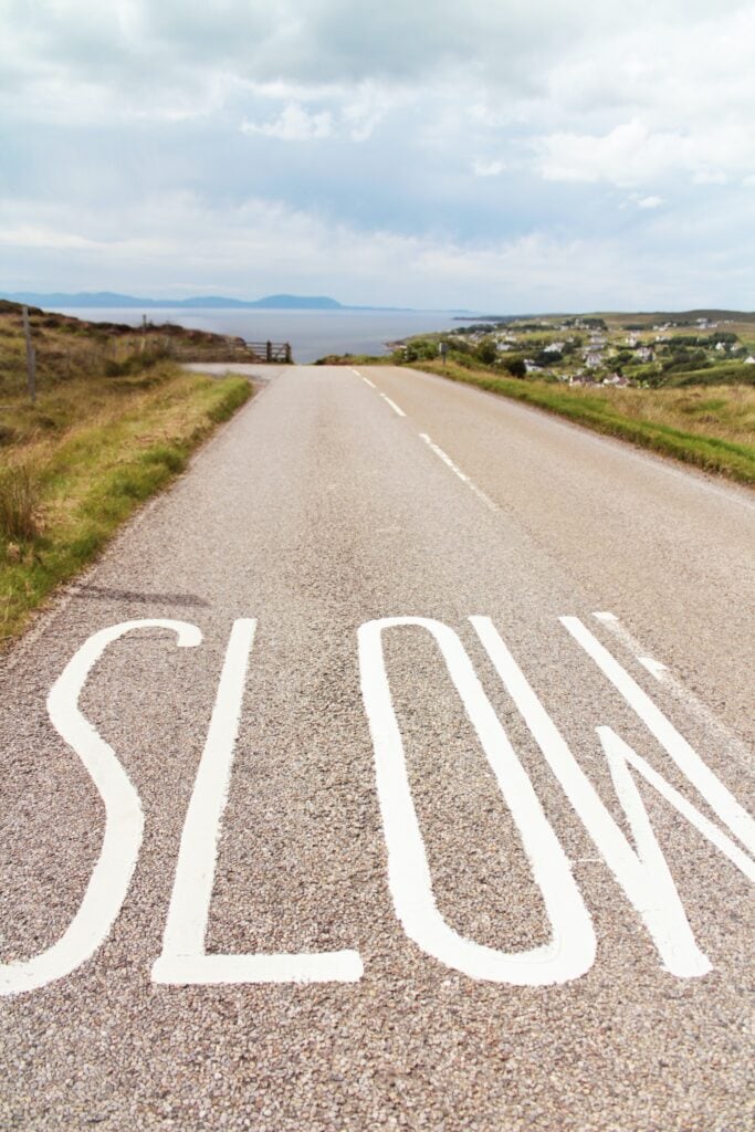 25 Pros and Cons of Living in Costa Rica in 2024 2 Road through the countryside that says "Slow" painted on the ground.